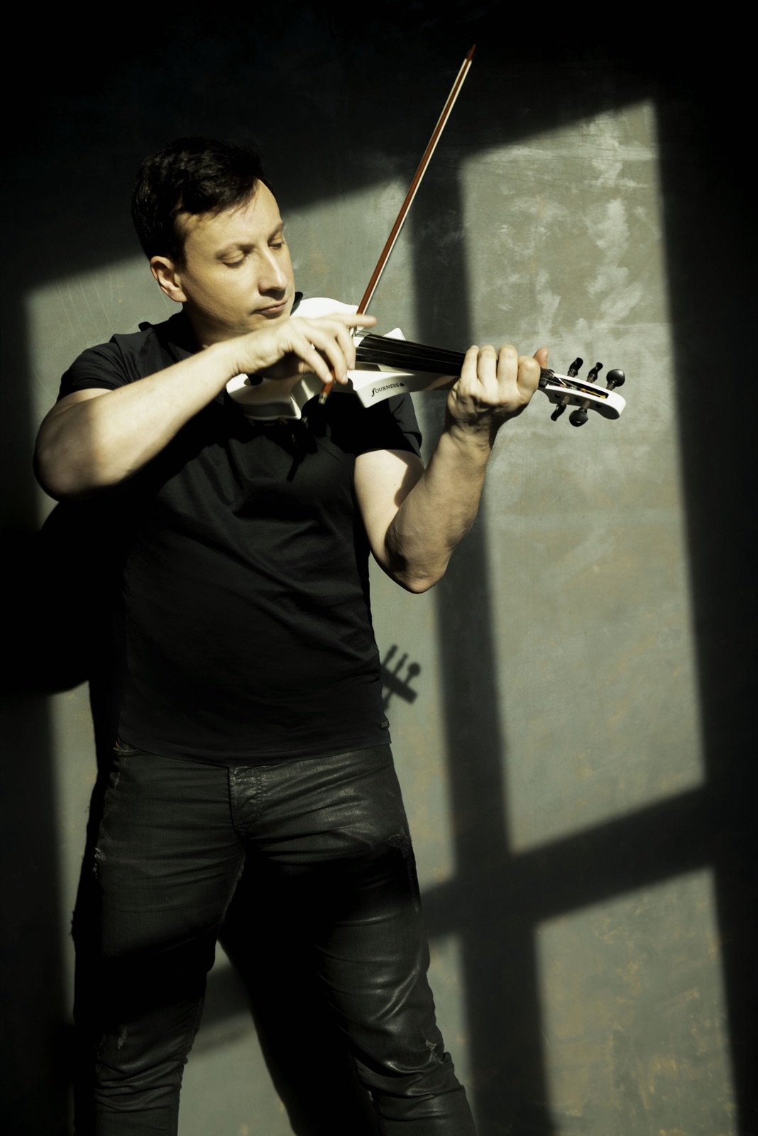 Fransoafran with a white electric violin against an industrial wall