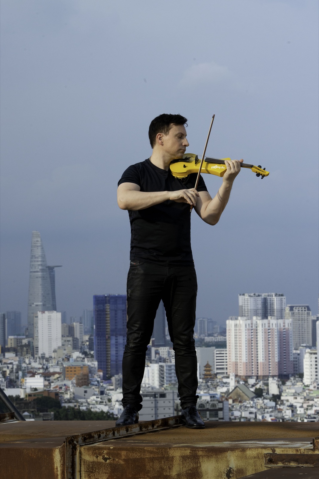 Fransoafran playing a yellow electric violin on a rooftop above Ho Chi Minh City